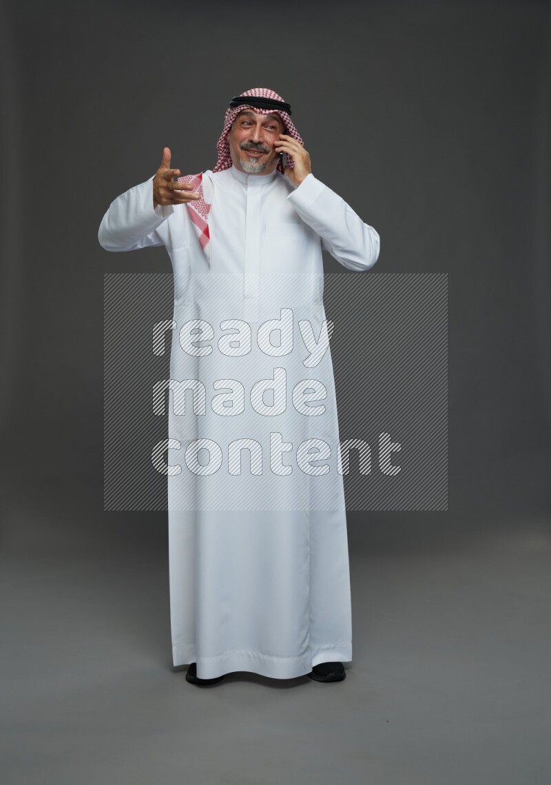 Saudi man with shomag Standing talking on phone on gray background