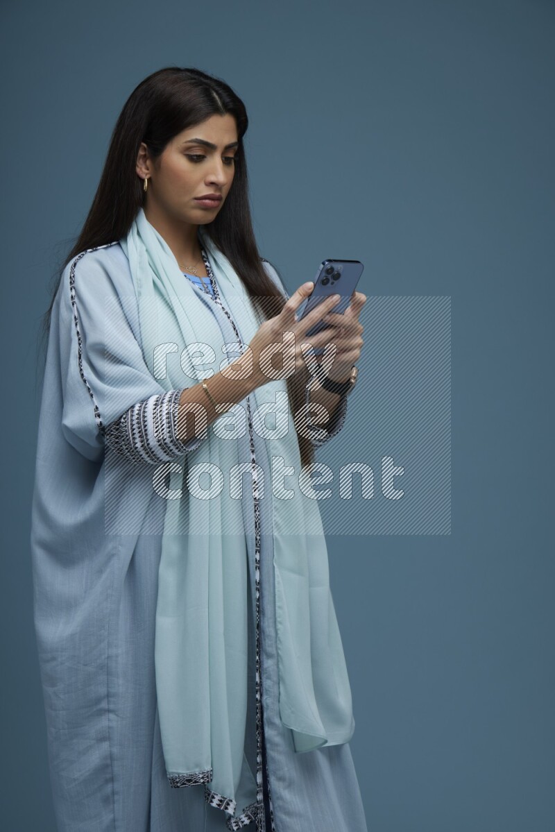 A Saudi woman Texting in a blue background wearing blue Abaya with no hijab