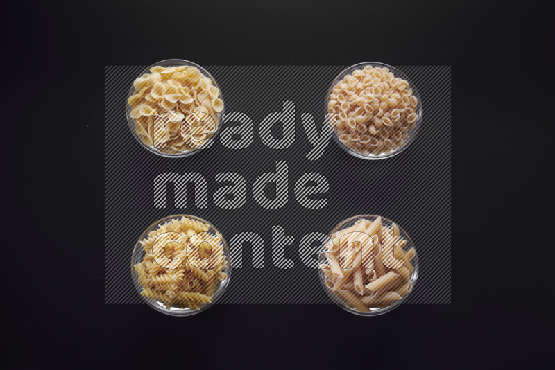 Different pasta types in glass bowls on black background