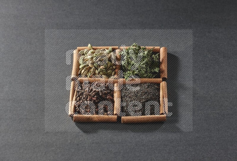 4 squares of cinnamon sticks full of black tea, cloves, dried mint leaves and cardamom on black flooring