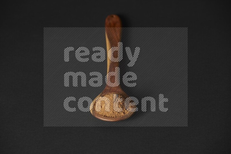 Cinnamon powder in a spoon ladle on black background
