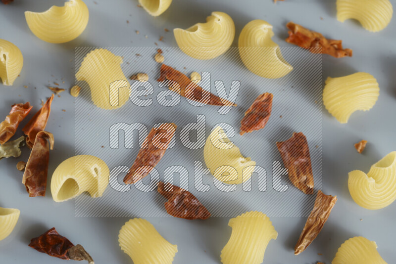 Raw pasta with different ingredients such as cherry tomatoes, garlic, onions, red chilis, black pepper, white pepper, bay laurel leaves, rosemary, cardamom and mushrooms on light blue background