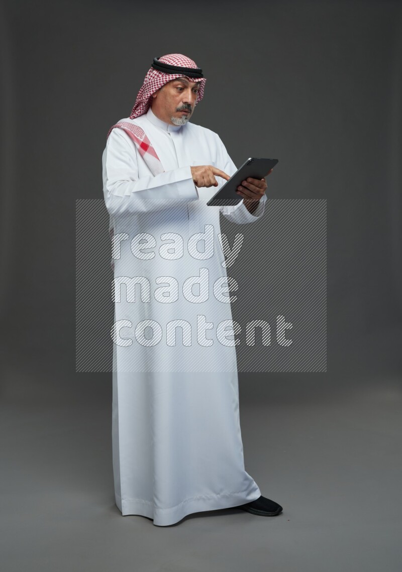 Saudi man with shomag Standing working on tablet on gray background