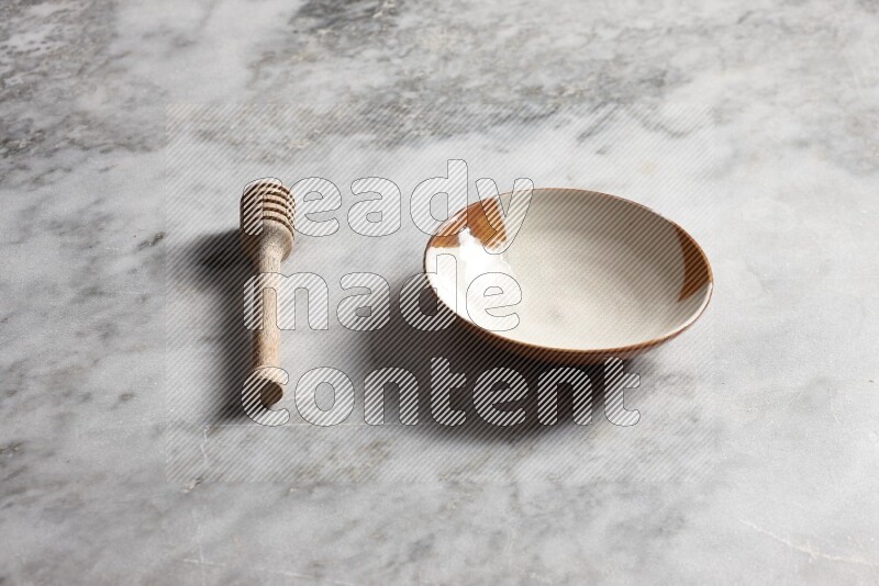 Multicolored pottery plate with wooden honey dipper on the side on grey marble background