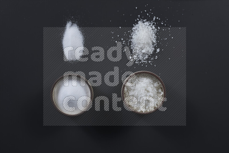 Pottery bowl full of fine table salt and coarse sea salt on black background