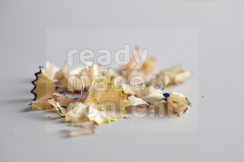 A close-up showing a small pile of pencil shavings with varied color edges on grey background