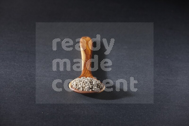A wooden ladle full of white pepper beads on black flooring