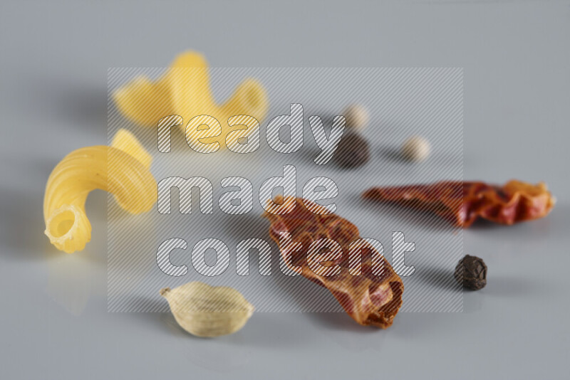 Raw pasta with different ingredients such as cherry tomatoes, garlic, onions, red chilis, black pepper, white pepper, bay laurel leaves, rosemary, cardamom and mushrooms on light blue background