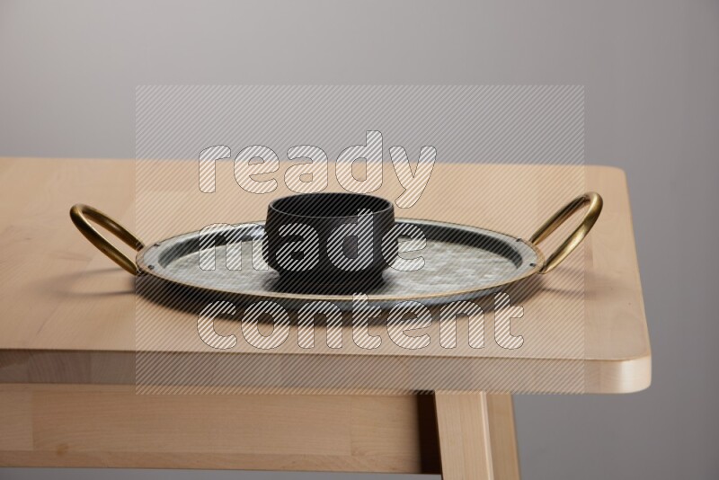 black bowl placed on a rounded stainless steel tray with golden handels on the edge of wooden table