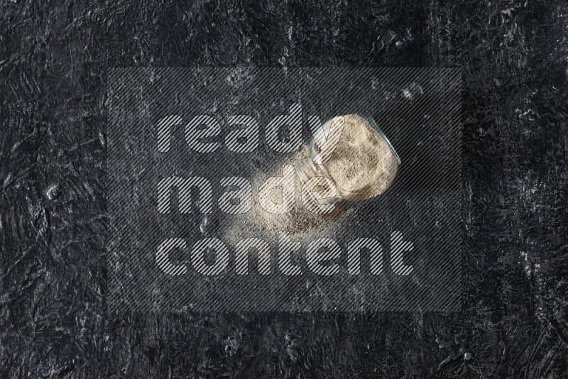 وعاء زجاجي عشبي مقلوب ممتلئ ببودرة الفلفل الأبيض مع بودرة متناثرة على أرضية سوداء