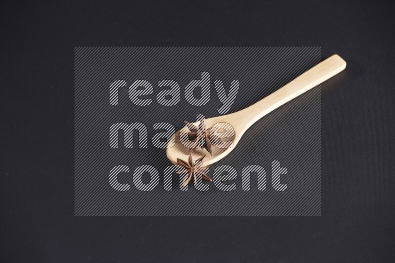 اليانسون النجمي في ملعقة خشبية فوق اليانسون النجمي الذي يغطي الإطار على أرضية سوداء