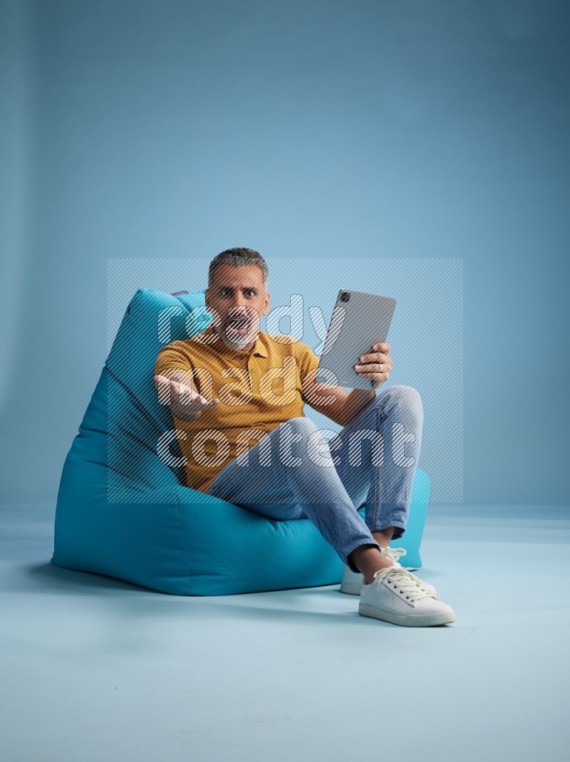 A man sitting on a blue beanbag and working on tablet