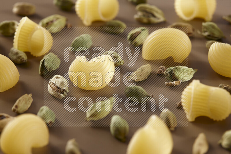 Raw pasta with different ingredients such as cherry tomatoes, garlic, onions, red chilis, black pepper, white pepper, bay laurel leaves, rosemary and cardamom on beige background