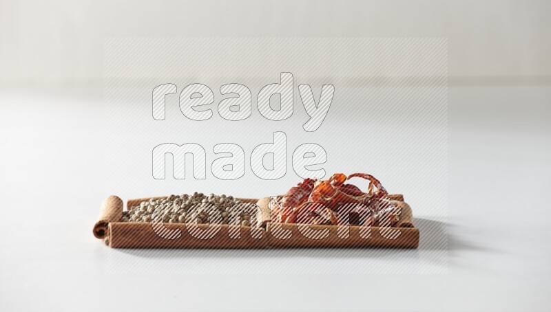 مربعان من أعواد القرفة ممتلئان بالفلفل الحار المجفف وحبوب الفلفل الأبيض علي خلفية بيضاء