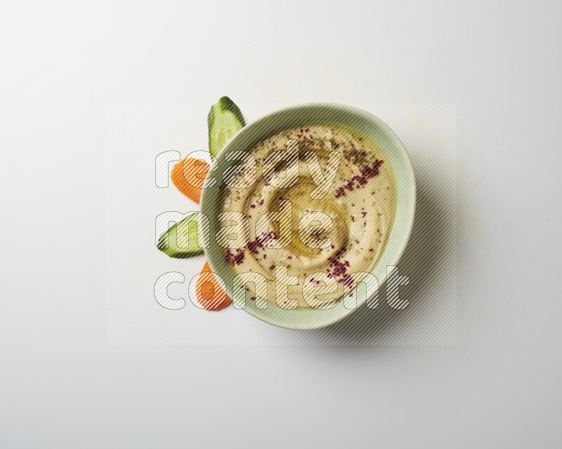Hummus in a green plate garnished with zattar & sumak on a white background