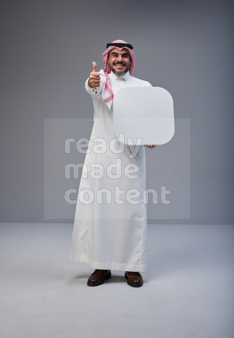 Saudi man Wearing Thob and red Shomag standing holding social media sign on Gray background