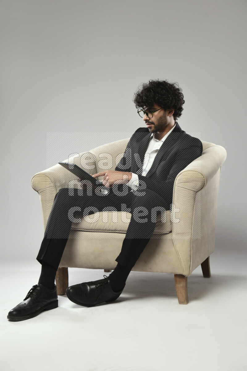 رجل يرتدي ملابس رسمية يجلس علي كرسي و يتصفح تابلت علي خلفية بيضاء