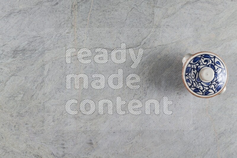 إناء فخاري متعدد الألوان مع غطائه على خلفية من الرخام الرمادي