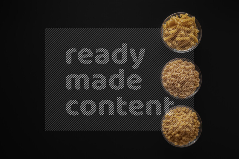 Different pasta types in 3 glass bowls on black background
