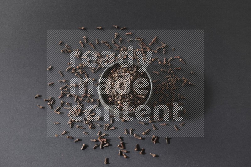 A black pottery bowl full of cloves on a black flooring