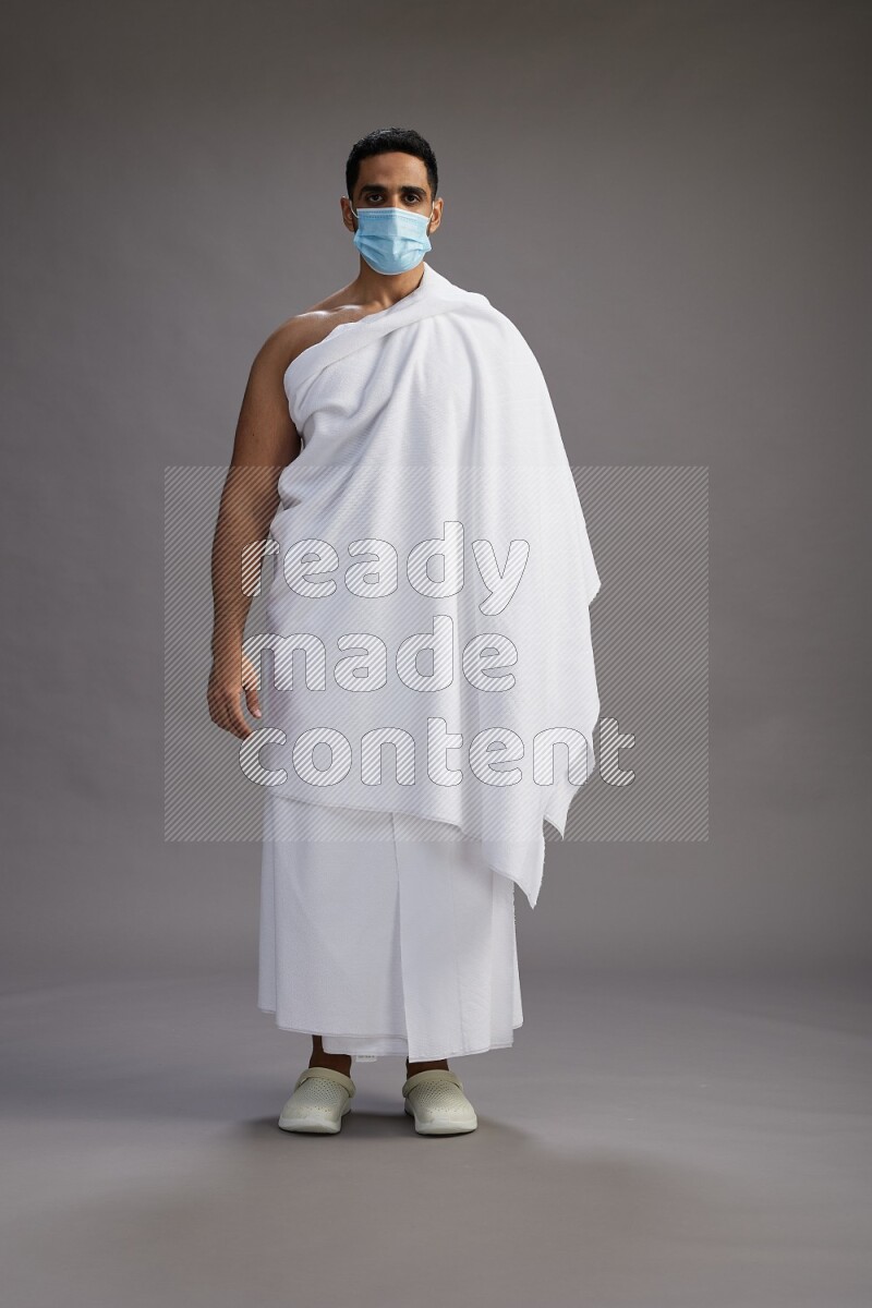 A man wearing Ehram with face mask Standing Interacting with the camera on gray background