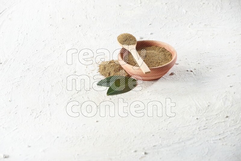 A wooden bowl and wooden spoon full of cumin powder on textured white flooring