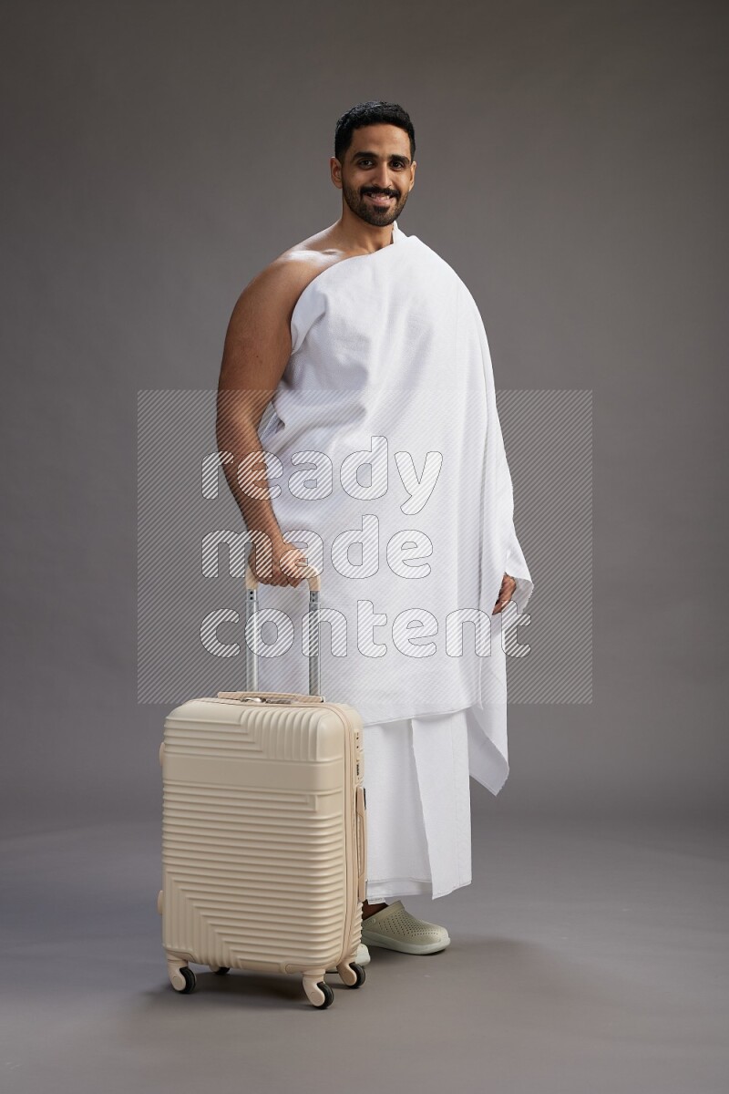 A man wearing Ehram Standing holding traveling bag on gray background