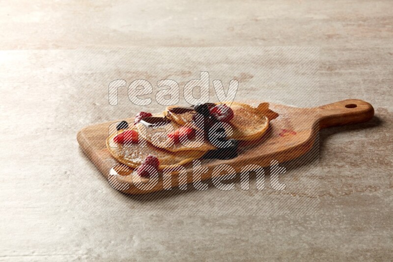 Three stacked mixed berries pancakes on a wooden board on beige background