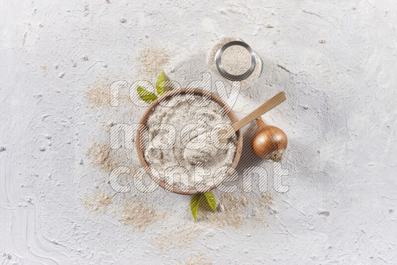A wooden bowl full of onion powder with a glass jar beside it and fresh onion on white background