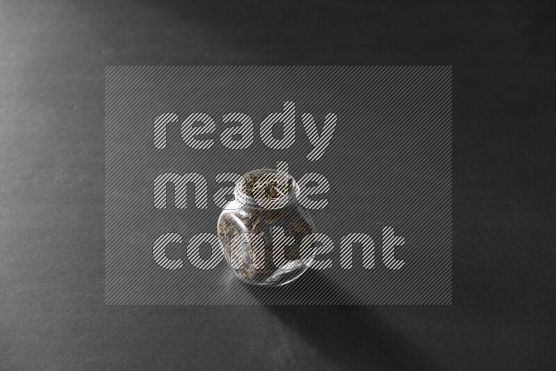 A glass spice jar full of basil on black flooring