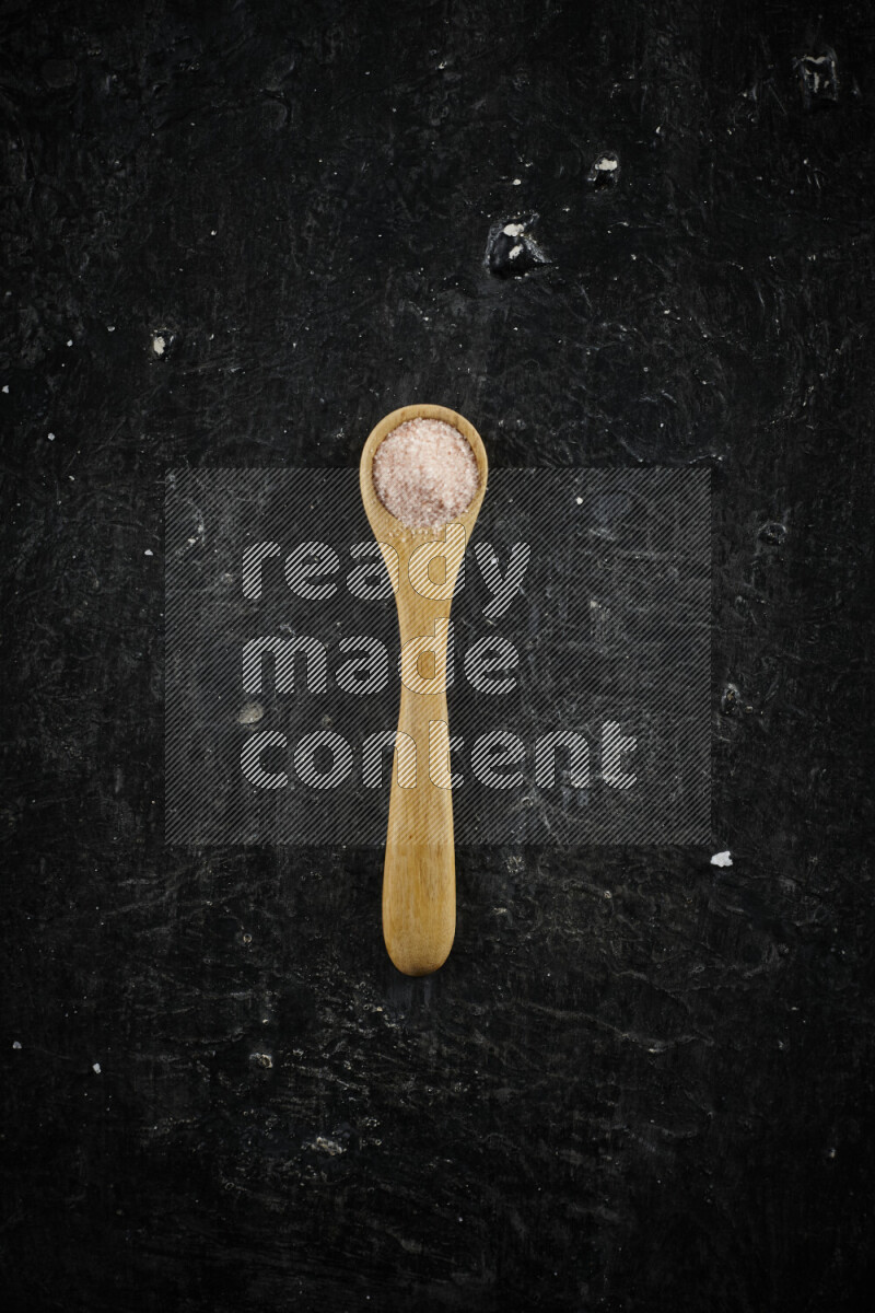 A wooden spoon full of pink himalayan salt on black background