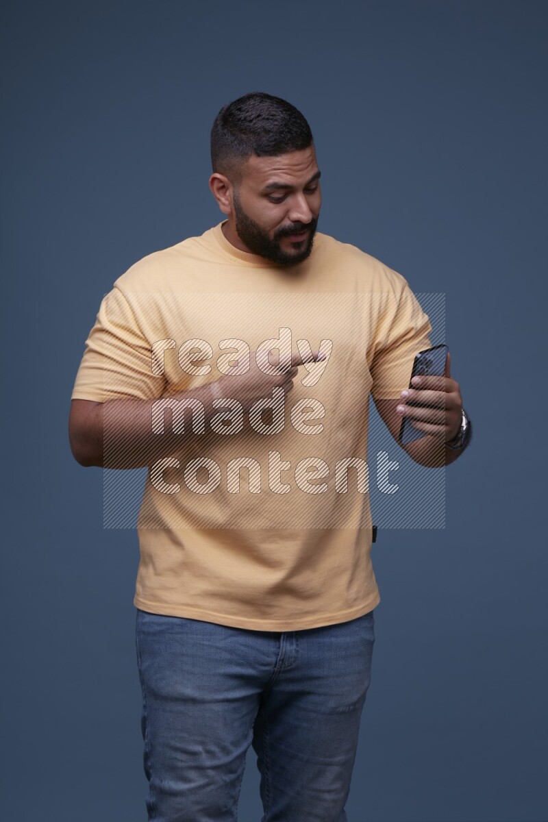 A man Pointing at a Smartphone on Blue Background wearing Orange T-shirt