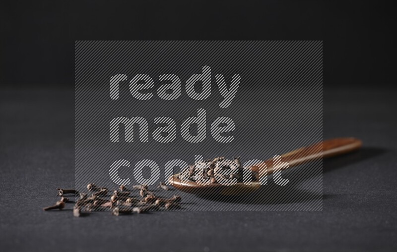 A wooden ladle full of whole cloves on a black flooring