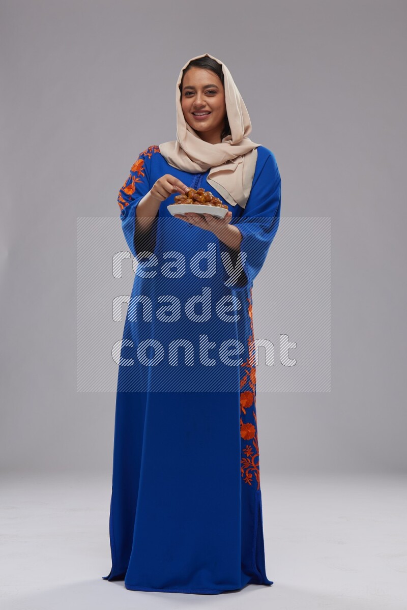 A Saudi woman standing wearing Jalabeya holding a plate of dates