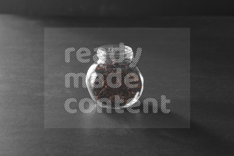 A glass spice jar full of cloves on black flooring