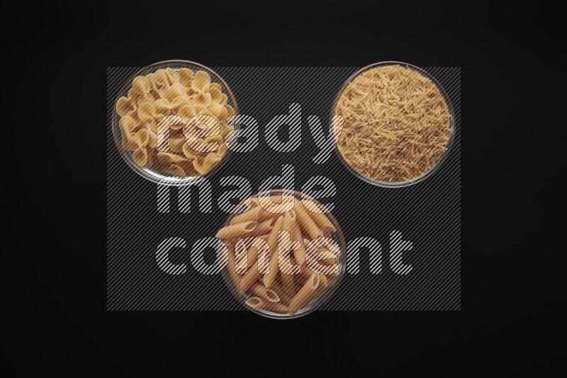Different pasta types in glass bowls on black background