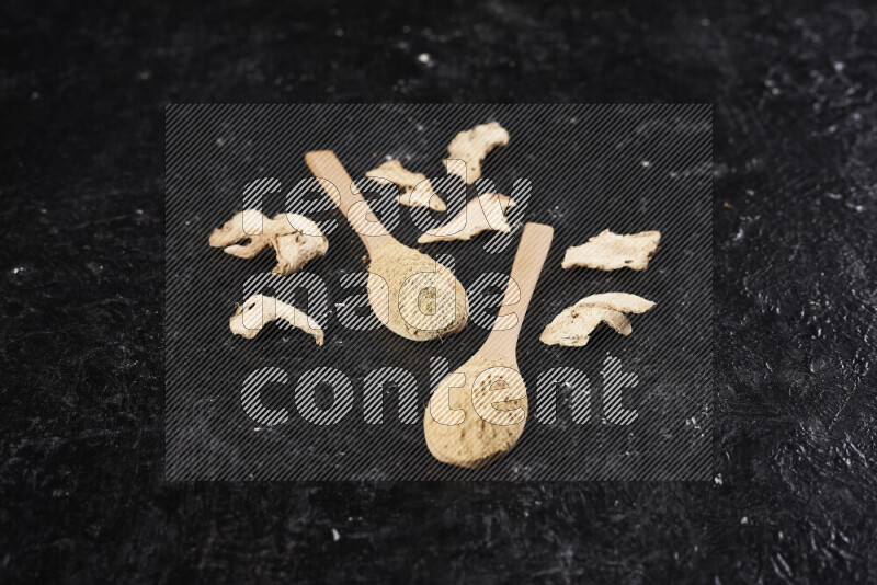 Two wooden spoons full of ground ginger powder on black background