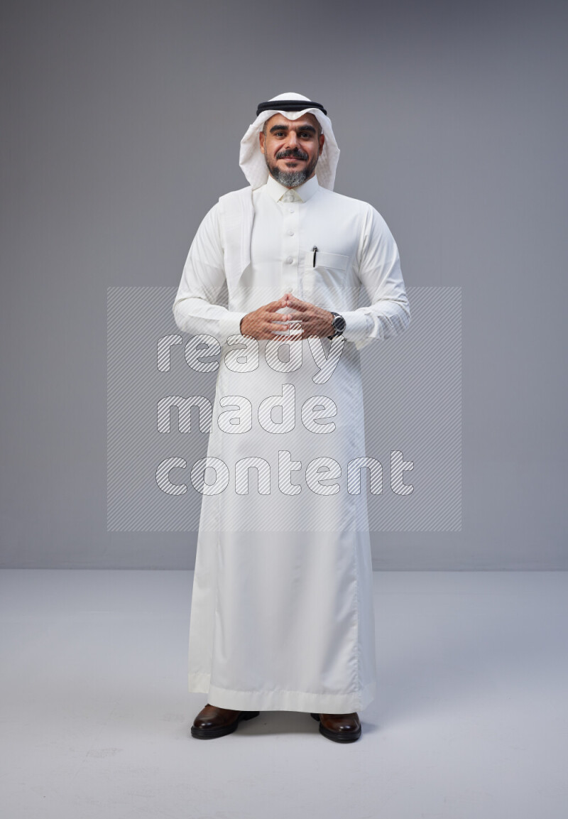 Saudi man Wearing Thob and white Shomag standing interacting with the camera on Gray background