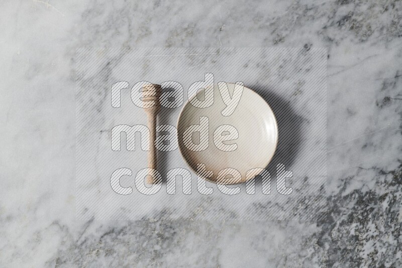Beige pottery plate with wooden honey dipper on the side on grey marble background
