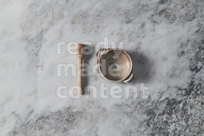 Multicolored pottery bowl with wooden honey dipper on the side on grey marble background