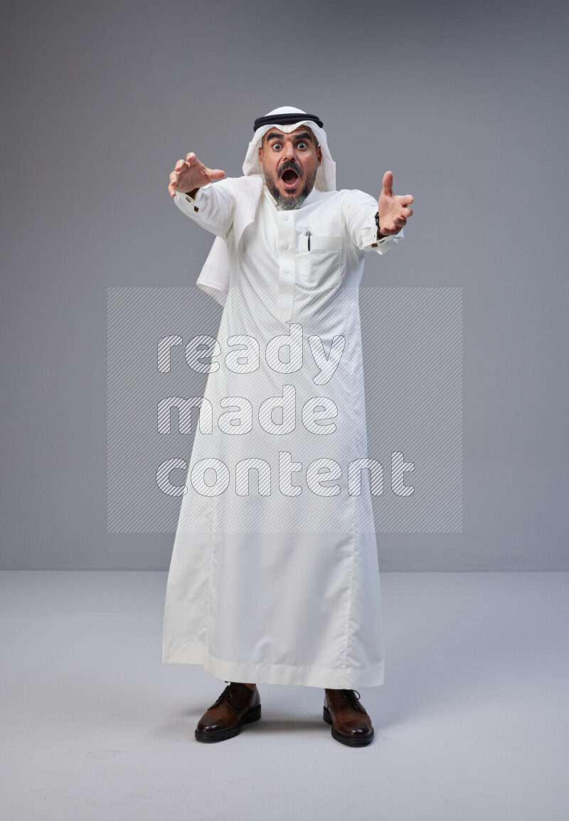 Saudi man Wearing Thob and white Shomag standing interacting with the camera on Gray background