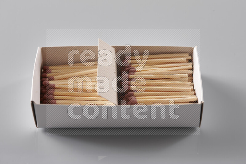 An open matchbox revealing wooden matches on a grey background