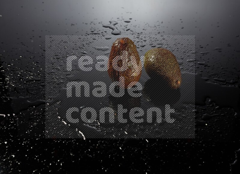 A whole avocado on black background with water drops.