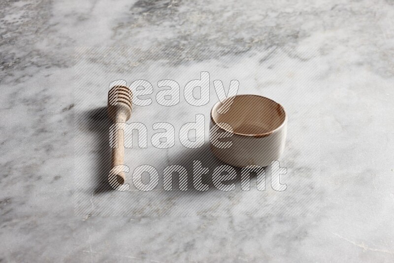 Multicolored pottery bowl with wooden honey dipper on the side on grey marble background