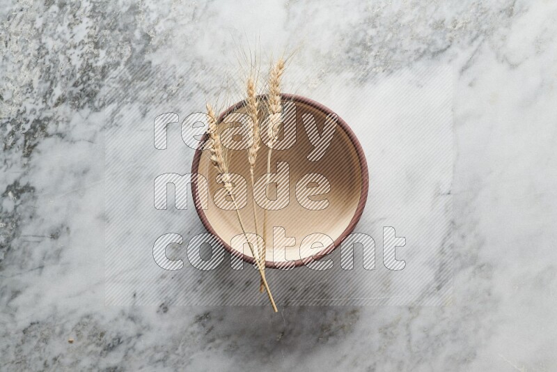 Wheat stalks on beige pottery oven bowl on grey marble background