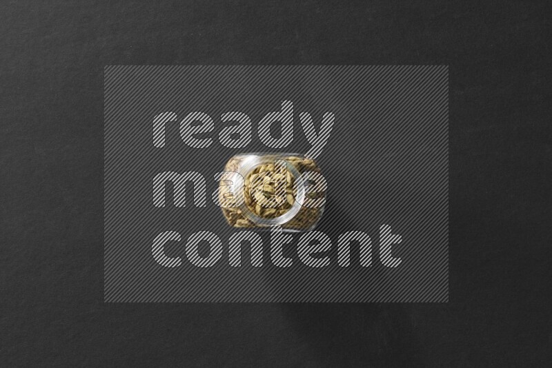 A glass spice jar full of cardamom on black flooring