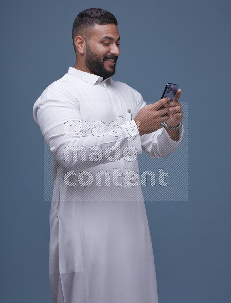 A man Texting on Blue Background wearing Saudi Thob