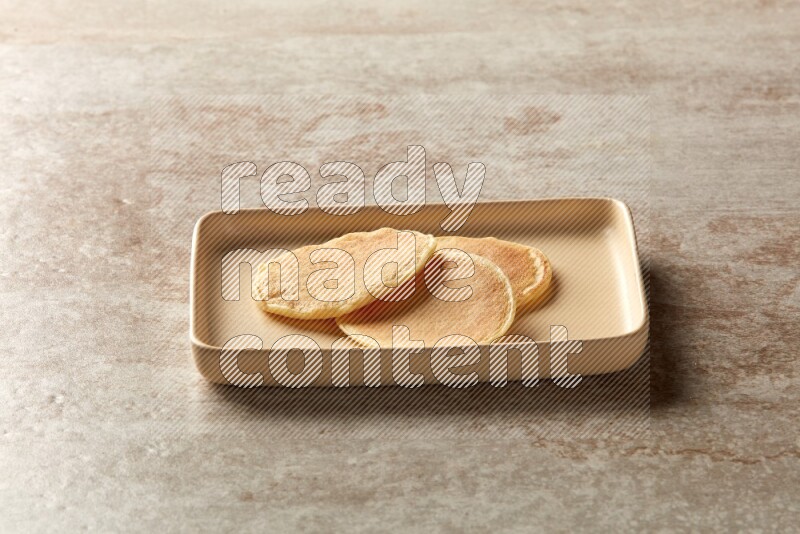 Three stacked plain mini pancakes in a rectangular plate on beige background