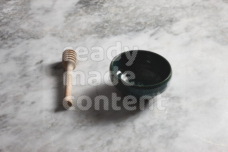 Dark green pottery bowl with wooden honey dipper on the side on grey marble background