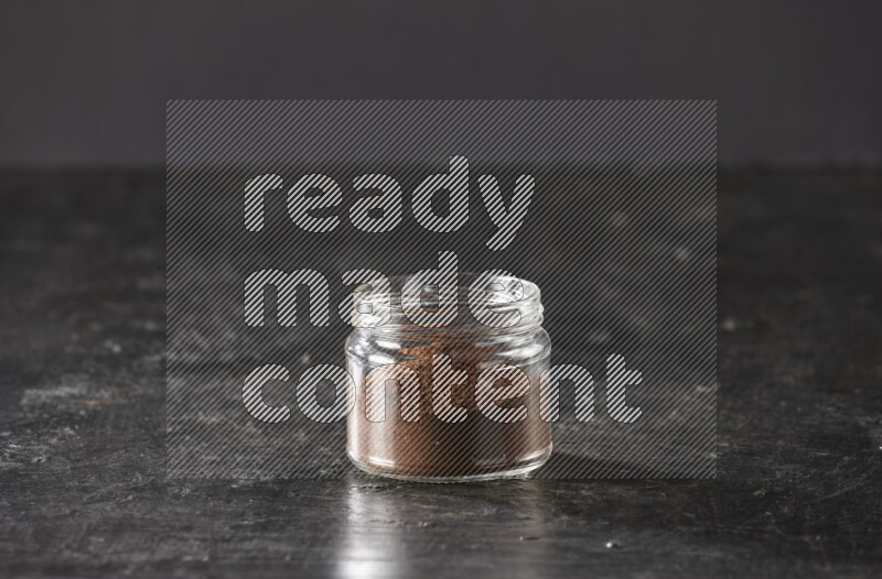 وعاء زجاجي ممتلئ ببودرة القرنفل على أرضية سوداء